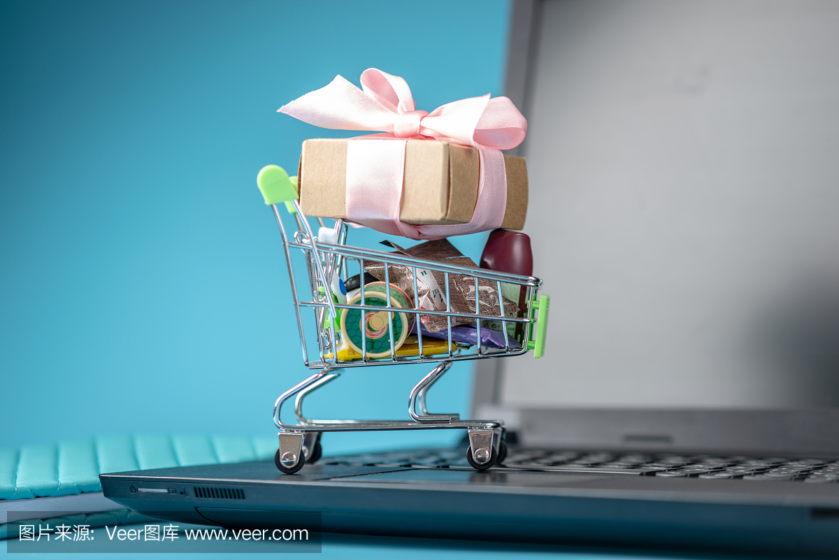 日常采购和礼物在购物车上的笔记本电脑键盘上的蓝色背景。网上购物
